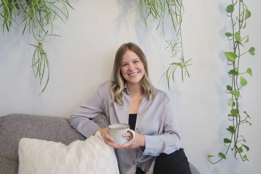 Maiah Horne, Registered Psychotherapist (Qualifying), smiling while sitting comfortably on a couch holding a mug.
