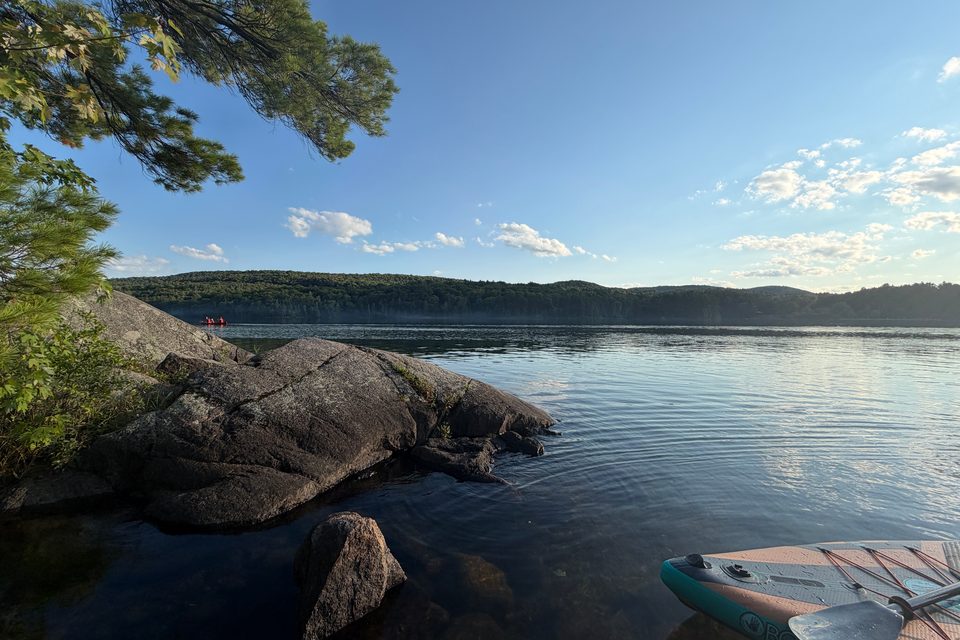 A calm lake beside granite rocks with a paddleboard at the shore.