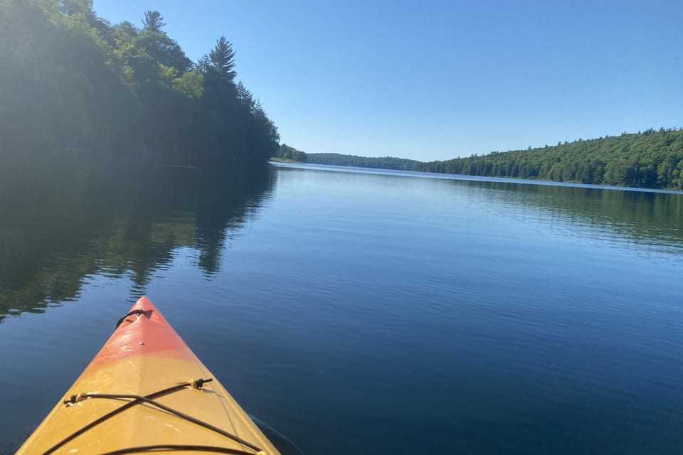The bow of a kayak on a calm, tree-lined lake.