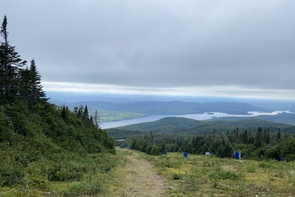 A mountain trail overlooking distant lakes and forest.