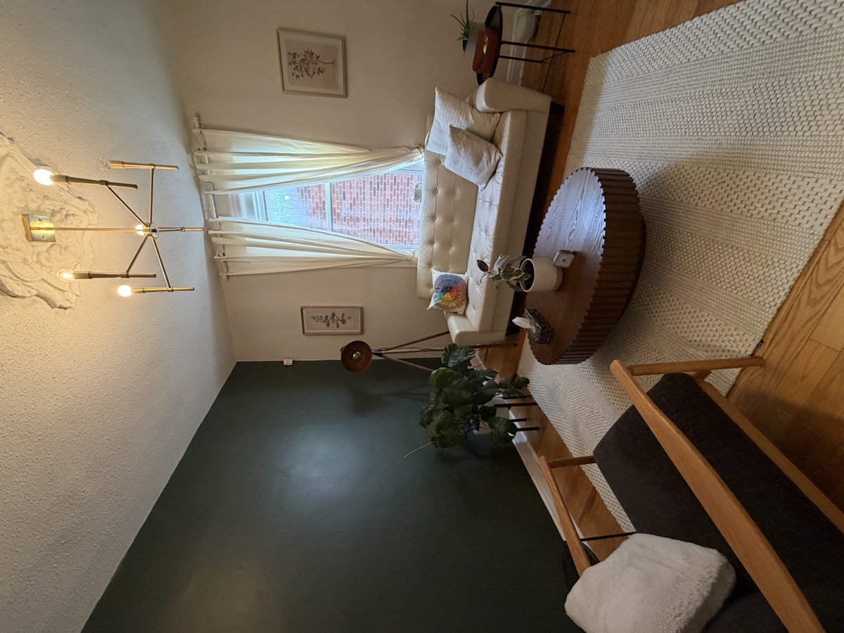 The Ripple Effect therapy room at 9 Melrose Ave: a calm space with a deep green accent wall, a cream couch by the window, plants, and soft lighting.