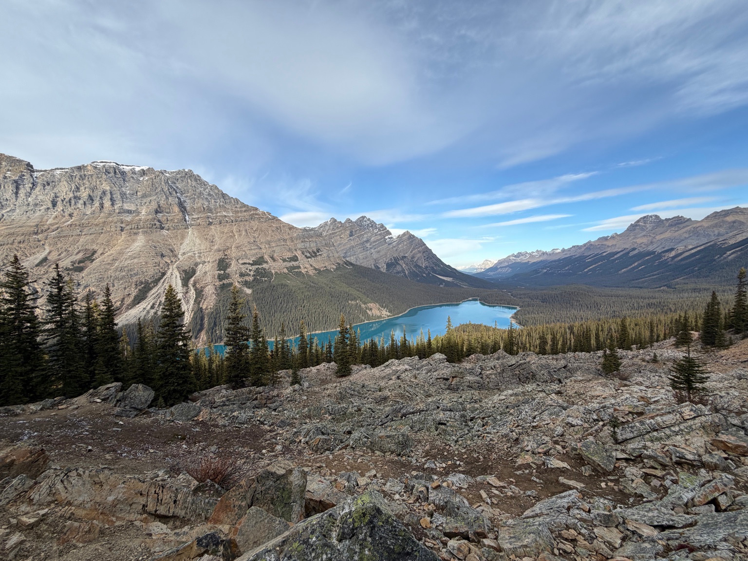 Turquoise lake surrounded by evergreen forest and rocky mountains beneath a blue sky.